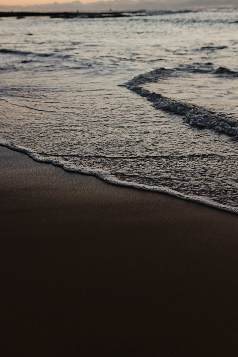 Foamy ocean waves wash onto the dark sand shore.