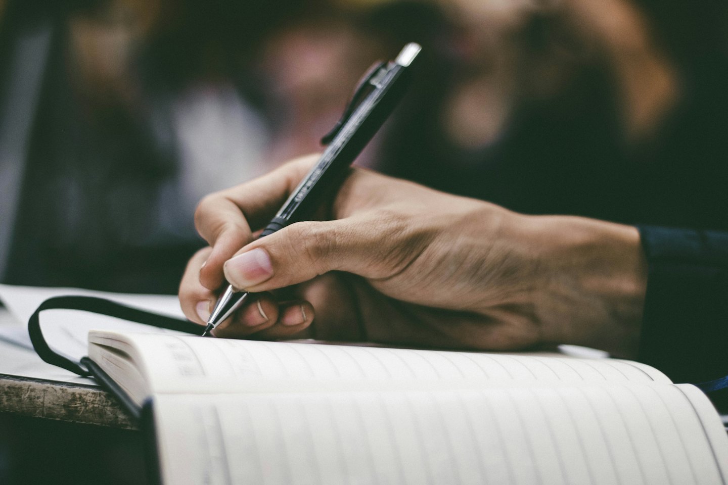 Person's hand writing notes in a notebook with a pen.